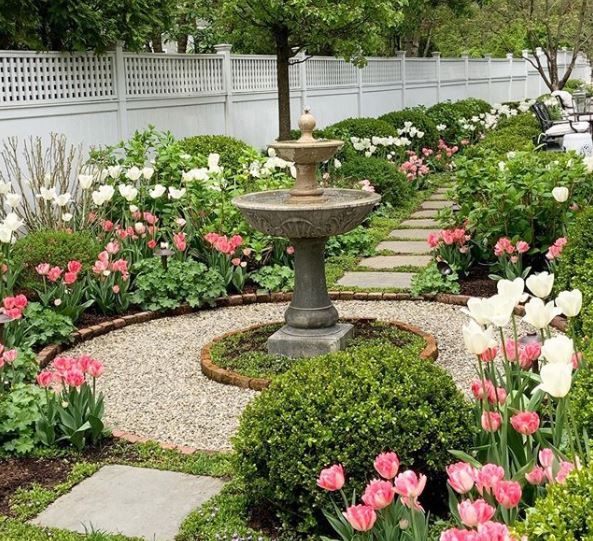 classical tiered water fountain in the centre of a gravel path surrounded by pretty flower beds