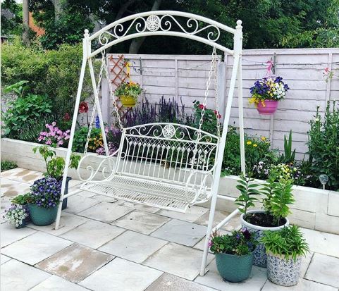 A white metal swing bench on a clean patio surrounded by flowers