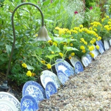 a flower bed edged with blue pattered ceramic plates in various sizes