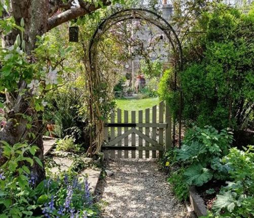 25 English Cottage Garden Ideas: Capture the Fairytale Charm 5 flowers grow over an archway across a pretty garden gate