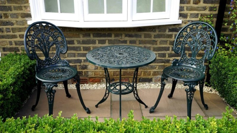 two intricate cast iron chairs either side of a matching table, on a small section of patio