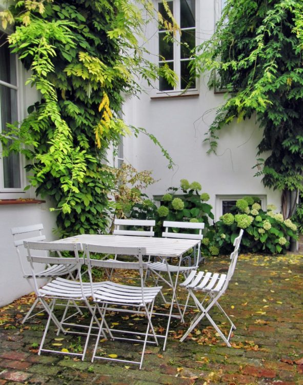 a white fold-up table with five fold-up chairs sitting in a leafy courtyard