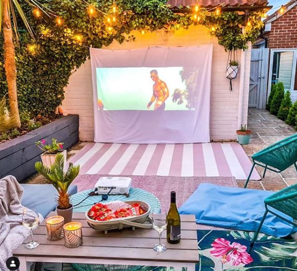 garden cinema screen made from a sheet on a shed, with a bowl of snacks and a bottle of wine