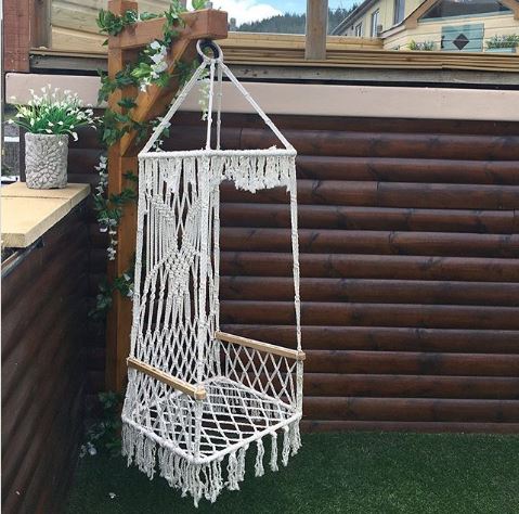 a macrame swing on a square base hanging from a beam