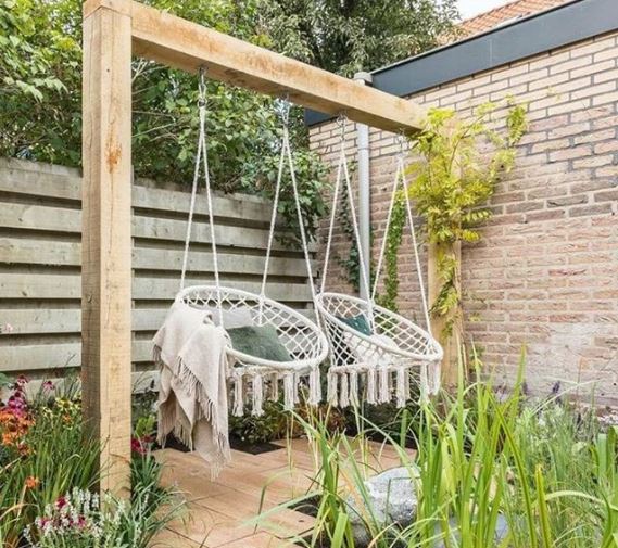 Two macrame garden swing chairs hand side by side on a wooden beam among plants