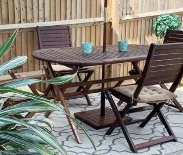 patio ideas using pale grey paving and an outdoor rug, beneath a wooden dining table and chairs