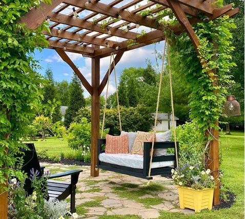 a rustic wooden bench hanging from a leaf-covered pergola