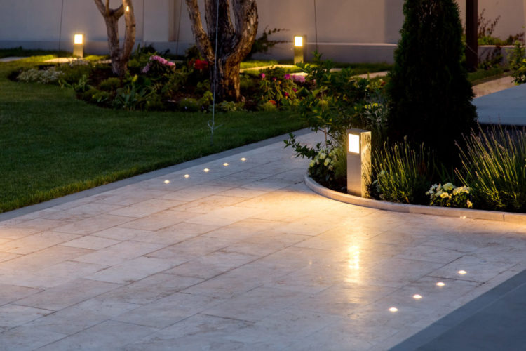 a glossy stone path with integrated spotlights and post lights shining from the flower beds