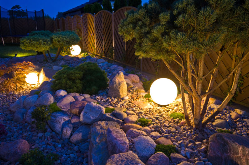 Spherical lights emitting a warm yellow glow in rocky flowerbeds