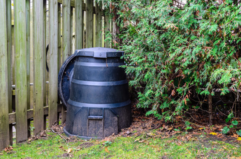 Bin Storage Ideas: How to Hide Your Wheelie Bins and Conceal Your Compost 6 a black plastic compost bin is tucked between a fence and large bush