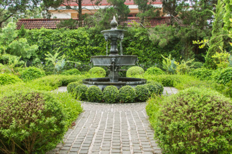 a paved path with a fountain and spherical topiary bushes in the middle