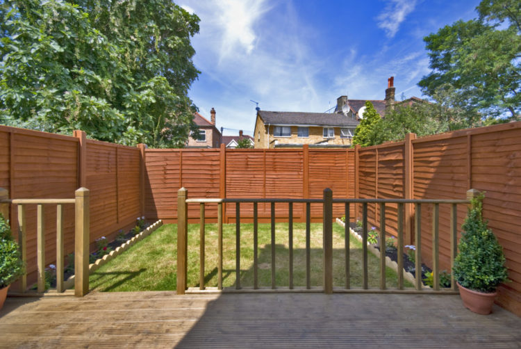 a simple rectangular garden with a deck and lawn with narrow floral borders and a sturdy looking fence