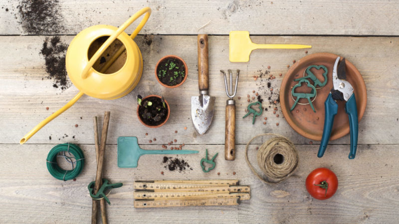 a flat-lay style image of garden tools including a watering can, trowel, fork and pots