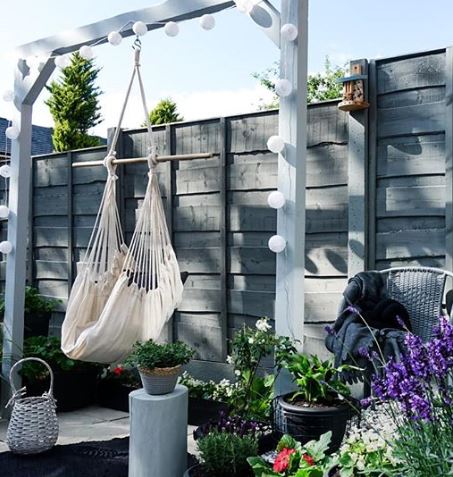 A white hammock hanging from a grey frame, which is decorated with little white paper lanterns on a string