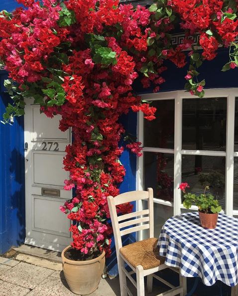 the front of a house painted royal blue, with white wood work and a table and chairs with blue checkered tablecloth.