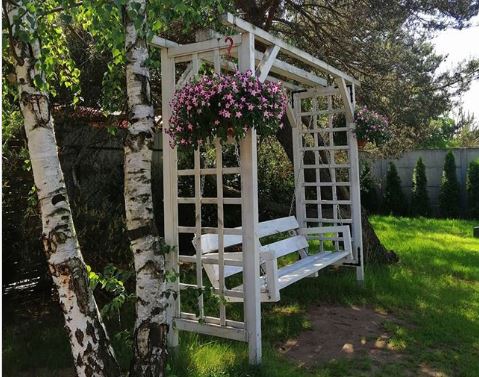 a white wooden swinging bench on a lawn, with pink flowers in hanging baskets
