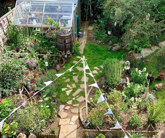 a stone patio that gradually thins out to become stepping stones in a garden with greenhouse and bunting