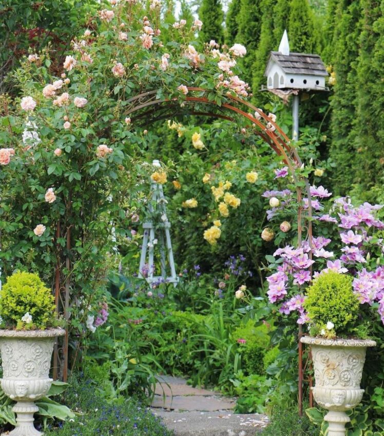 a rose-covered arbour flanked by stone planters
