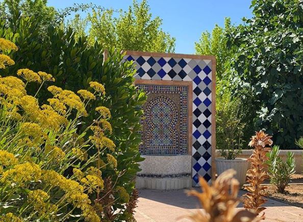 a busy garden with a tiled archway surrounding a small fountain