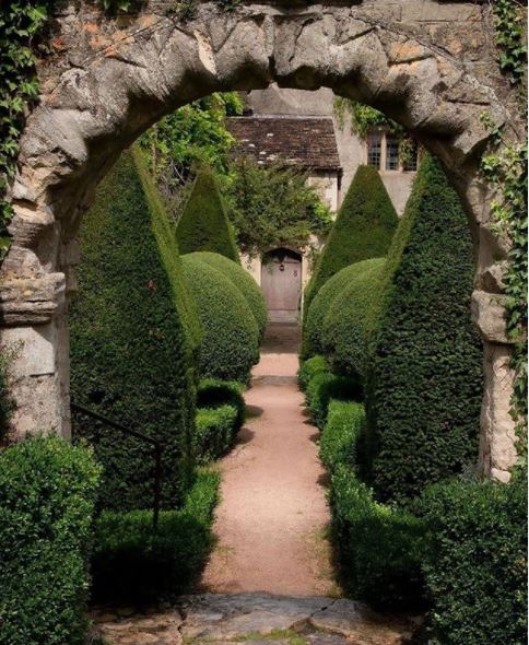 an archway with a row of elaborate topiaries behind it