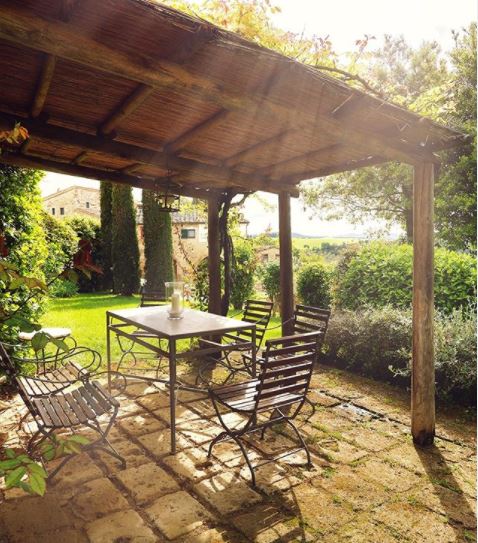 a shady pergola above a mossy patio with garden furniture