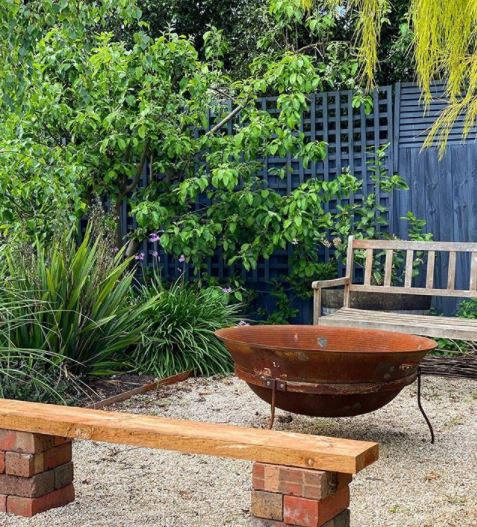 29 Garden Fire Pit Ideas for Cosy Evening Get-Togethers 22 a rust coloured metal fire bowl in a simple, homely patio area