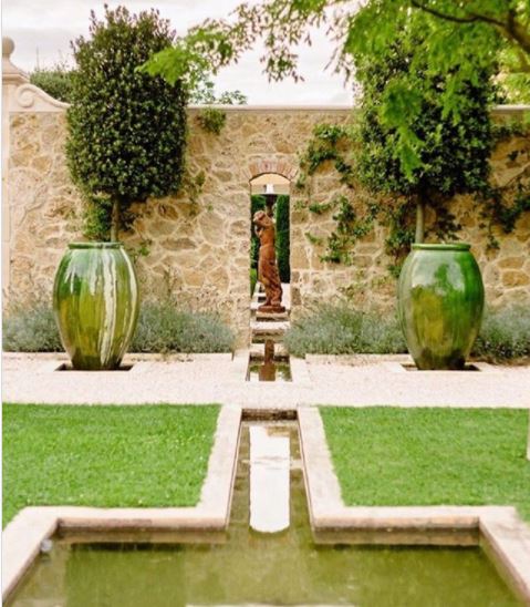 two large green pots flank a bronze scultpture in a symmetrical italian style garden with pond