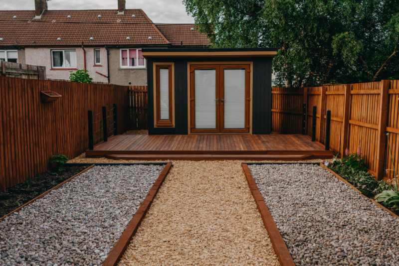 a minimalist shed painted black and brown in a gravel garden