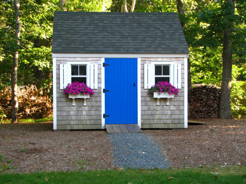 40 Garden Shed Ideas for Pretty to Practical Outdoor Buildings 15 a grey shed with blue door, white window shutters and purple flowers