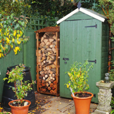 a green shed with log storage in the corner of a garden