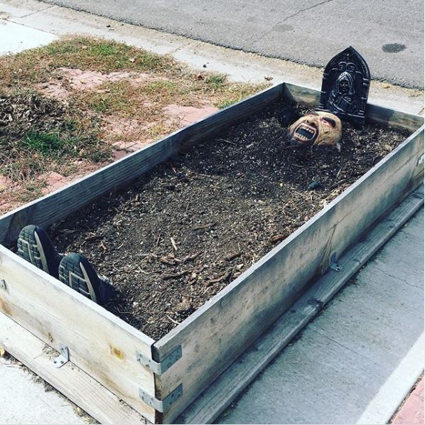 22 Halloween Garden Ideas: Fun & Low-cost Spooky Decorations 2 a raised planter with shoes and a mask poking out the soil to look like a spooky grave
