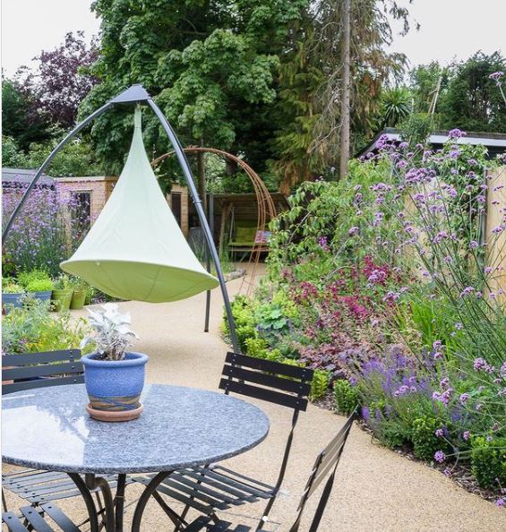 a garden with lots of brightly coloured flowers, a gravel path and a swing seat
