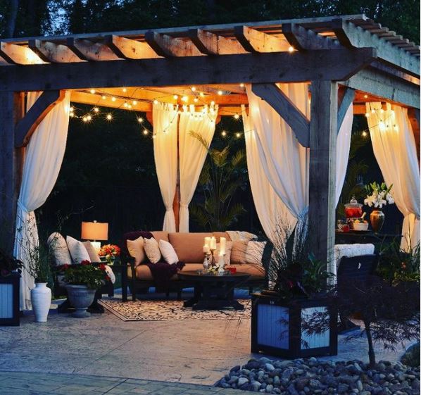 a gazebo with curtains covering comfy outdoor seating with cushions and candles