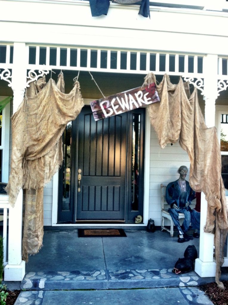 22 Halloween Garden Ideas: Fun & Low-cost Spooky Decorations 6 a house porch decorated with stained sacks and a sign that says "beware"