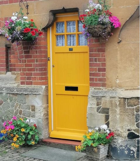 a cheerful yellow door with hot pink flowers in hanging baskets either side