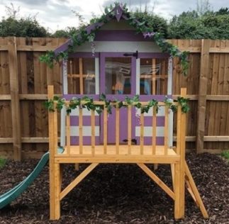 a playhouse painted with purple and cream stripes, on a raised platform with steps and a slide
