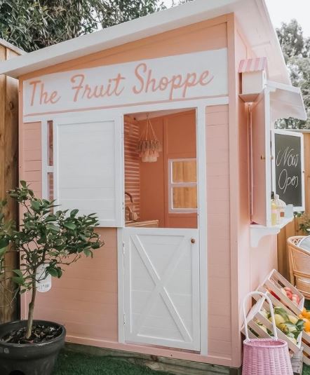 a peach coloured shed with a hand-painted sign that reads "the fruit shoppe" with a counter and pretend goods for sale