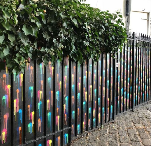 29 Unique Garden Mural Ideas for Outdoor Walls & Fences 4 a black fence with sprayed-on paint circles of blue, red, turquoise and yellow