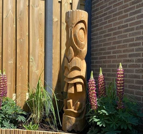 a small wooden tiki carving in a flower bed