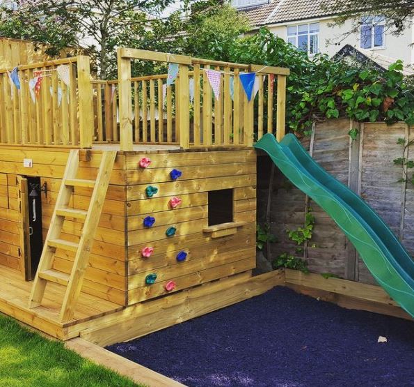 a big, boxy playhouse with a ladder and climbing wall up to a lookout-deck with a slide