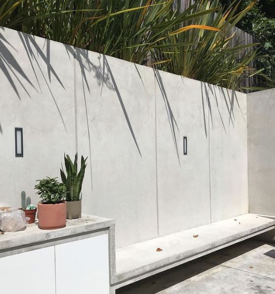a concrete structure creates a seat, storage unit, wall and planter along the edge of a garden