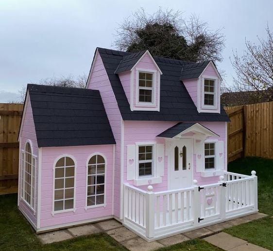 a huge pink playhouse with a front deck and what appears to be an extension with lots of windows