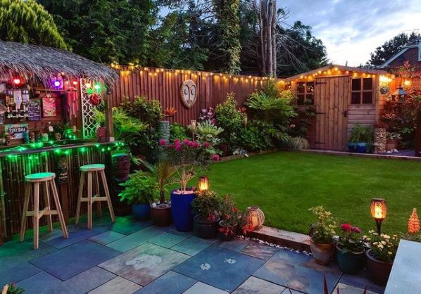 a UK garden with tiki garden ideas like a stone patio, wooden mask, exotic plants and tiki bar