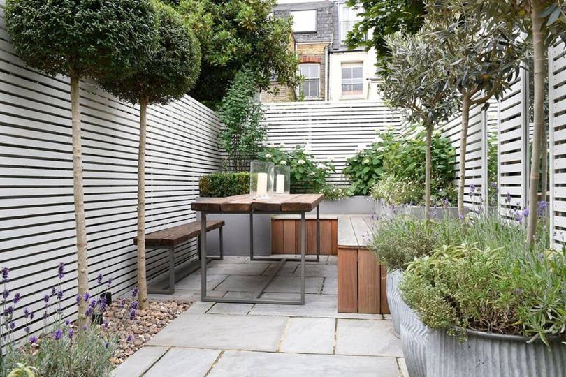 a small narrow garden with horizontally slatted fences and skinny trees