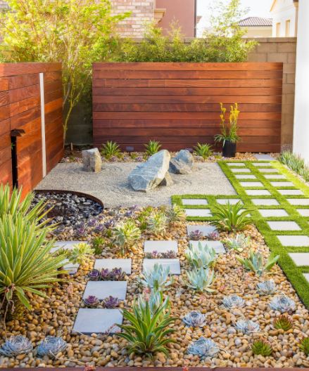 a small garden with a rockery, a strip of grass, a fountain and a tiny zen garden