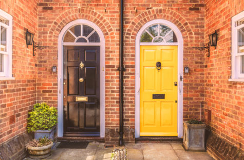 the entrances to two side-by-side terrace homes, with freshly painted doors and symmetrical lights, planters and brackets for hanging baskets.