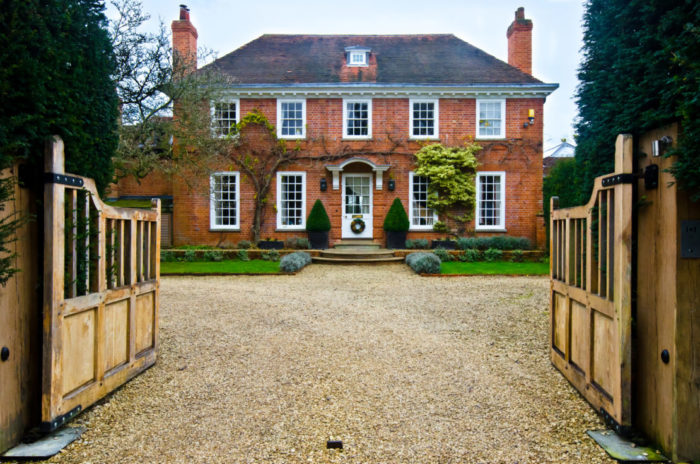 double gates opening into a long gravel driveway leading to a large country house