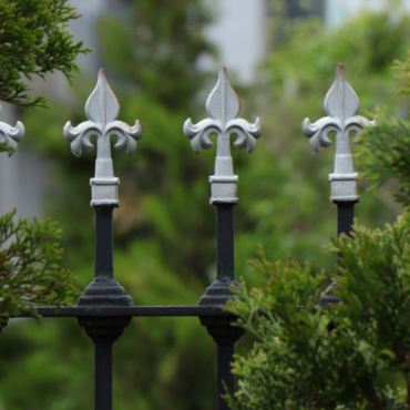 a black, iron fence with a silver Fleur-de-lis at the top of each bar