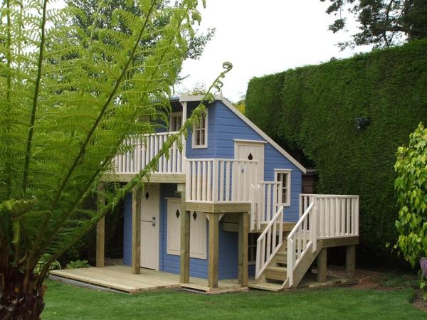 a two-storey playhouse with a set of wooden stairs leading to a separate door on the second level