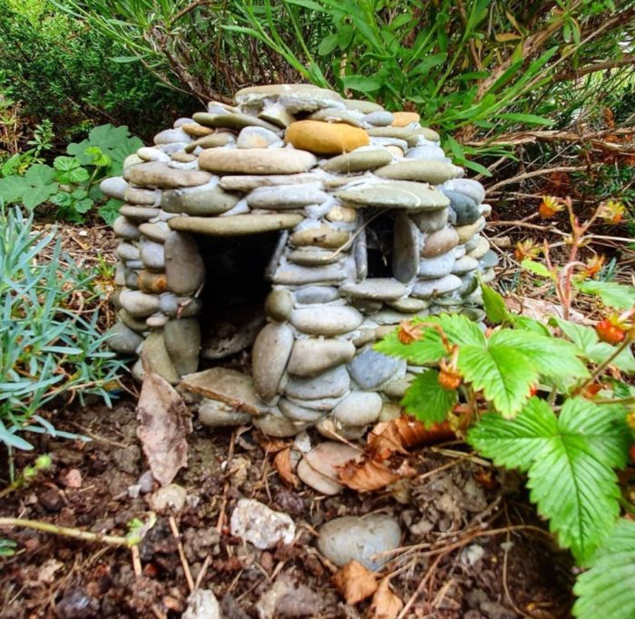 a tiny house made from pebbles nestled in the undergrowth of a garden